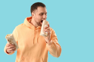 Yakışıklı genç adam mavi arka planda lezzetli donör kebabı yiyor.