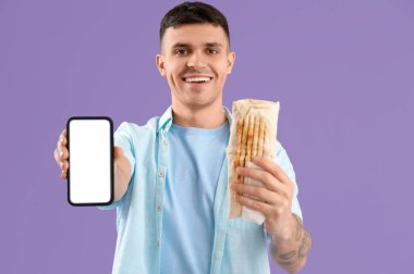 Lezzetli bir donör kebabı ve eflatun arka planda cep telefonu olan yakışıklı bir genç.