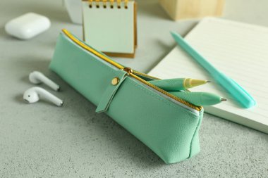 Yeşil kalem kutusu, kalemler, defter ve kulaklıklar gri arka planda.