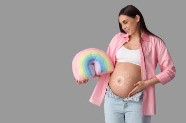 Karnında kremadan yapılmış güneş kremi ve açık arkaplanda gökkuşağı yastığı olan hamile bir kadın.