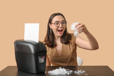 Mutlu sekreter bej arkaplanda kağıt öğütücüsünde belgeyi yok ediyor