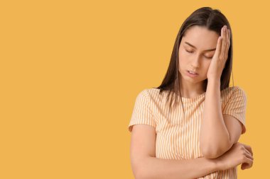 Sarı arka planda baş ağrısı çeken yorgun genç bir kadın.