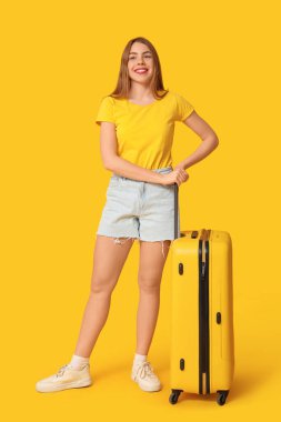 Arka planda sarı valizi olan güzel genç bir kadın.