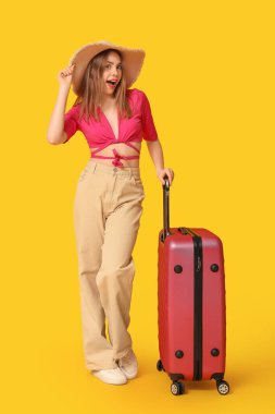 Beautiful young woman with suitcase on yellow background