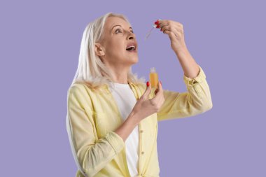 Olgun bir kadın leylak arka planında CBD yağı kullanıyor.