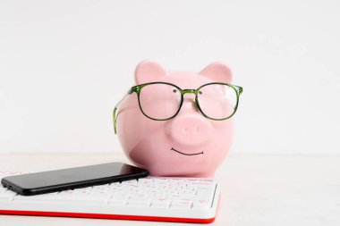 Cep telefonu ve klavyesi beyaz arkaplanda olan domuz kumbarası