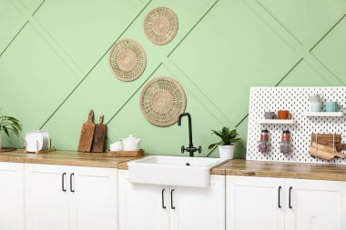 Tahta, lavabo ve beyaz tezgahlar mutfaktaki yeşil duvarın yanında.