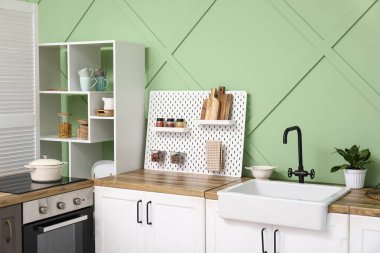 Tahta, beyaz tezgah ve askı modern mutfağın içindeki yeşil duvarın yanında.