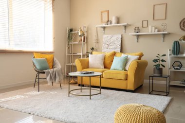 Sarı kanepesi, halısı, koltuğu, halısı ve sehpası olan şık bir oturma odası.