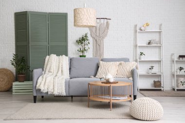 Gri kanepe, raf ünitesi, lamba ve sehpası olan aydınlık oturma odasının içi.