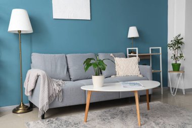 Rahat kanepe, çiçek, lamba ve sehpası olan mavi oturma odasının şık bir iç mekanı.