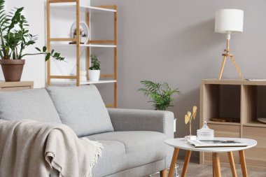 Oturma odasında rahat bir kanepe, çiçekler, raf ünitesi ve kahve masası var.