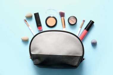 Mavi arka planda makyaj ürünleri, süngerler ve fırçalar bulunan kozmetik çanta