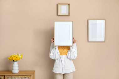 Şık bir odada narsisli vazonun yanında resim çerçevesi tutan genç bir kadın.