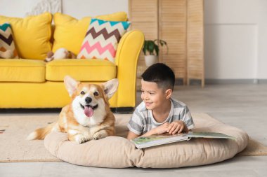 Little happy Asian boy reading book with cute Corgi dog at home