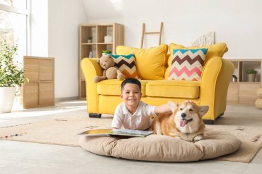 Little happy Asian boy reading book with cute Corgi dog at home