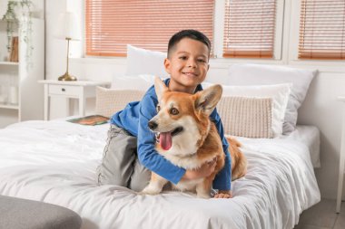 Küçük mutlu Asyalı çocuk ve tatlı Corgi köpeği evde yatakta oturuyor.