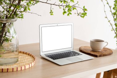 Şık bir iş yeri, bir fincan kahve, dizüstü bilgisayar ve aydınlık oturma odasında çiçek açan dalları olan vazo.