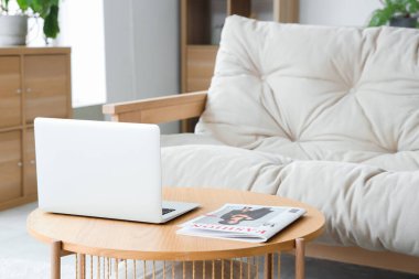 Oturma odasındaki ahşap masada dergi olan dizüstü bilgisayar, yakın plan.