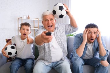 Babası ve dedesiyle birlikte oturma odasında TV 'de futbol maçı seyreden bir çocuk.