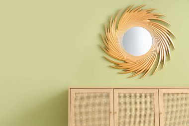 Odanın yeşil duvarında ahşap dolap ve şık bir ayna.