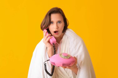 Sarı arka planda battaniyeli genç ve güzel bir kadın telefonla konuşuyor.