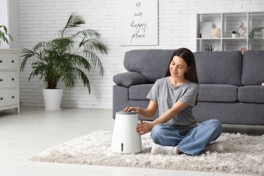 Genç bir kadın oturma odasındaki modern nemlendiriciyi açıyor.