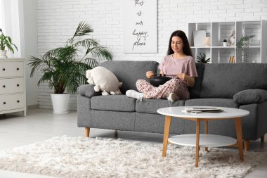 Oturma odasındaki kanepede glukofon çalan genç bir kadın.