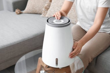 Genç kadın rahat koltukta oturuyor ve modern nemlendiriciyi açıyor şık oturma odasında, yakın plan