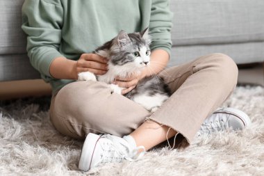 Uzun saçlı tatlı kedisi olan genç bir kadın oturma odasında yerde oturuyor.