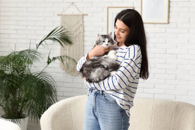 Genç bir kadın oturma odasında uzun saçlı sevimli bir kedi tutuyor.