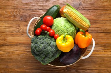Tahta arka planda farklı taze sebzelerle dolu bir sepet.