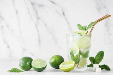 Beyaz arka planda limonlu, naneli ve şekerli bir bardak taze mojito kokteyli.