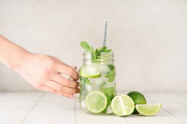 Beyaz arka planda bir kavanoz taze Mojito kokteyli ile kadın eli.