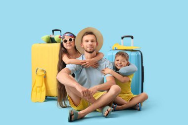 Mavi arka planda oturan küçük çocukları ve bavullarıyla mutlu bir baba. Seyahat kavramı