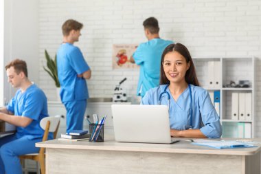 Klinikteki masada dizüstü bilgisayarla çalışan Asyalı kadın doktor.