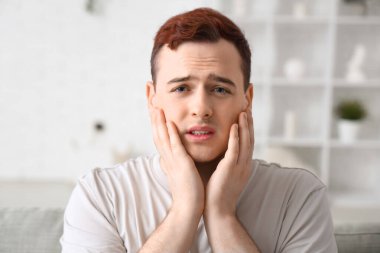 Genç adam odada diş ağrısı çekiyor.
