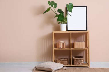 Salonda bej duvarın yanında ev bitkisi ve resim çerçevesi olan raf ünitesi