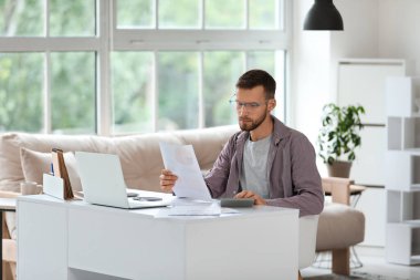 Gözlüklü genç işadamı iş yerinde modern bilgisayarlı belgeler tutuyor.