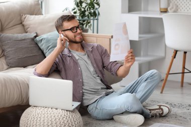 Gözlüklü genç işadamı cep telefonuyla konuşuyor ve ofiste belgelerle çalışıyor.