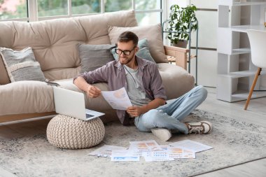 Gözlüklü genç işadamı ofiste yerde doküman ve bilgisayarla çalışıyor.