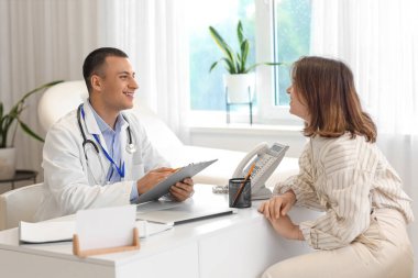 Klinikteki masada hastayla çalışan yakışıklı doktor.