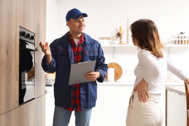 Erkek teknisyen müşteriyle mutfakta elektrikli fırının yanında çalışıyor.
