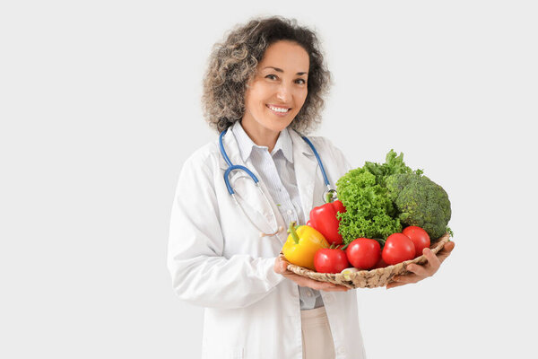 Зрелая женщина-диетолог со здоровыми овощами на светлом фоне