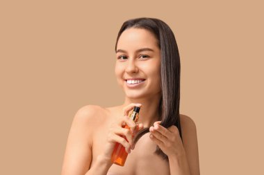 Young woman with cosmetics for hair treatment on beige background clipart