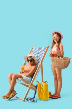 Mayo giymiş şirin çocuklar, meyve suyu bardaklı güneş gözlükleri, paletler ve mavi arka planda güneş şezlongu.