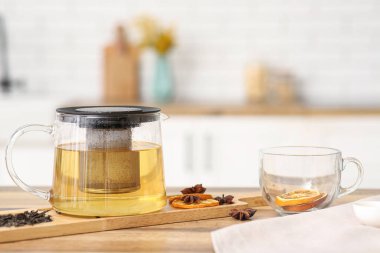 Çaydanlık ve bir fincan yeşil çay, yanında yıldız anason ve mutfaktaki masada bir dilim limon.