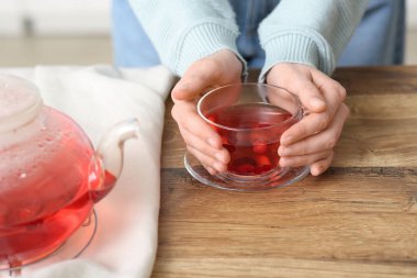 Genç bir kadın mutfakta yaban mersini çayıyla fincanı tutuyor.