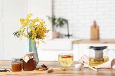Çaydanlık ve bir fincan yeşil çay. Mutfaktaki masada bir kavanoz bal ve mimoza.