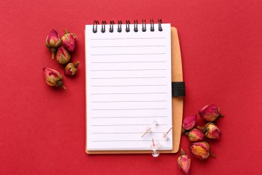 Kırmızı arka planda kurumuş gül çiçekleri ve defter kompozisyonu